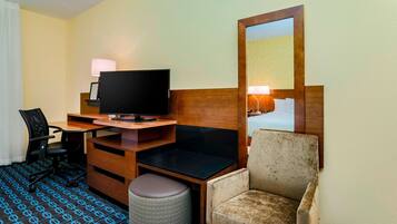 A hotel room with a desk, chair, television, and a large mirror.
