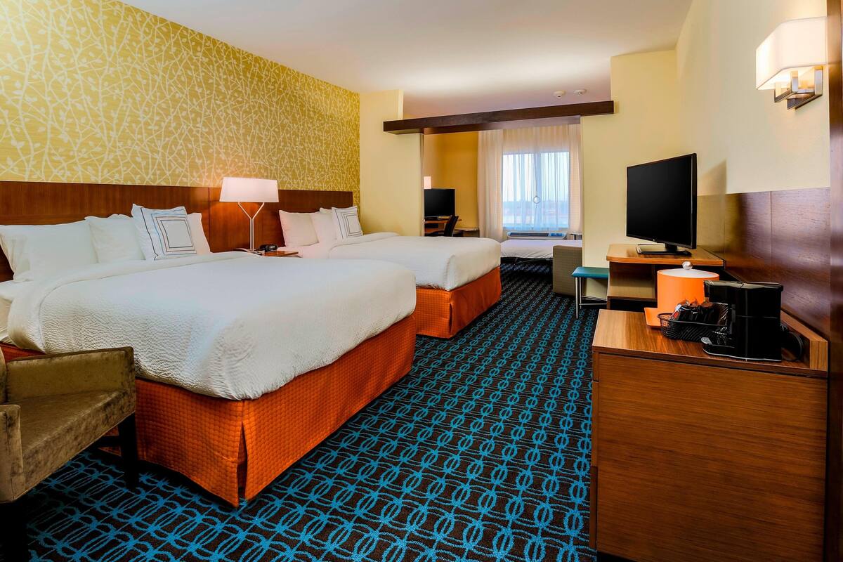 A hotel room with two beds, a desk, a TV, and a patterned carpet.