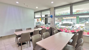 A restaurant with multiple tables and chairs, large windows with a view of parked cars and a building outside. - Beauty Trip Hotel (Taichung)