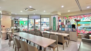 A modern restaurant interior with a long dining table, multiple chairs, and a view of the street through large windows. - Beauty Trip Hotel (Taichung)
