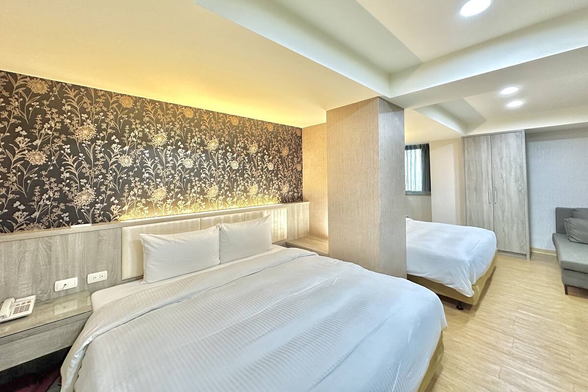 A hotel room with a large bed, a bedside table with a phone, a wardrobe, and a seating area.