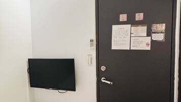 Una habitación con cama, un televisor de pantalla plana en la pared y una puerta con varios avisos.