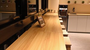 Een lange houten bank met een fotolijst ertegen, een keuken met een spoelbak en een waterdispenser, en een spiegel die de ruimte weerspiegelt.