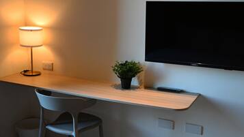 A modern room with a wooden desk, a chair, a small potted plant, a lamp, and a mounted TV.