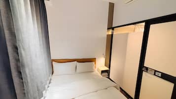 A hotel room with a bed, a nightstand, a wall-mounted air conditioner, and a window with curtains.