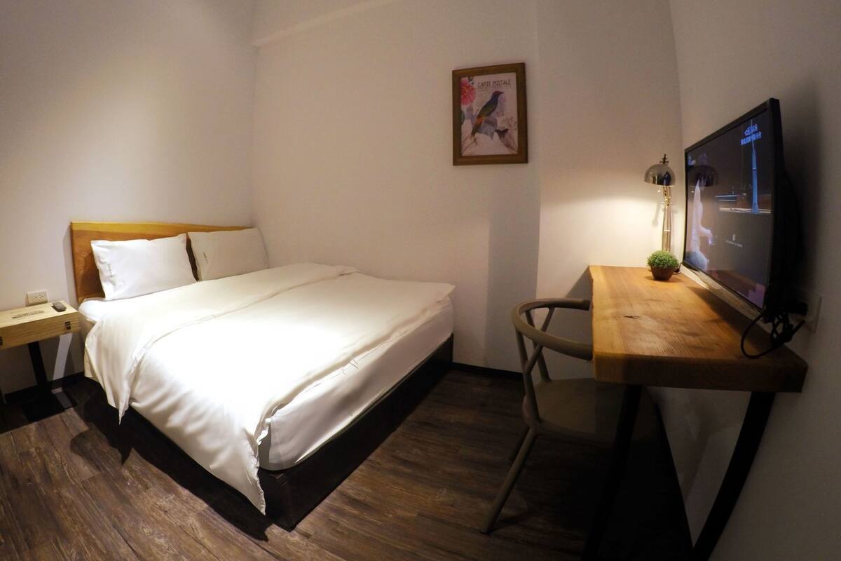 Une chambre à coucher avec un lit, une table de chevet, une lampe, une télévision et une petite plante.
