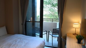 Een hotelkamer met een bed, een bureau met lamp en uitzicht op het omliggende landschap door een schuifdeur.