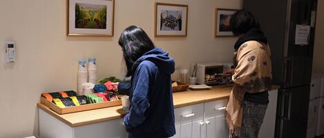 A kitchen area with a counter displaying various packaged goods, a refrigerator, and two framed pictures on the wall.
