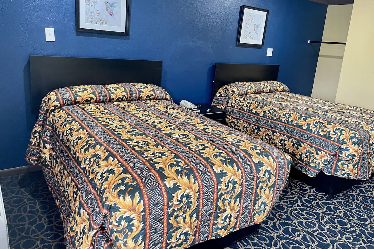 A hotel room with two beds, each with patterned bedding, a large headboard, and framed artwork on the walls.