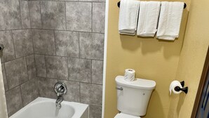 A bathroom with a bathtub, toilet, and a towel rack with towels. - Super 6 Inn (Carencro)