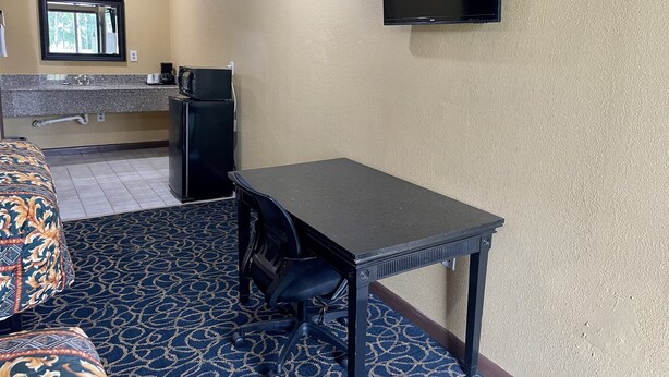 A compact hotel room with a kitchenette, a small table with a chair, and a television mounted on the wall. - Super 6 Inn (Carencro)