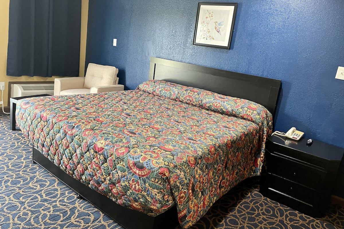 A hotel room with a bed, a chair, a dresser, and a framed picture on the wall.