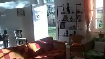 A living room with a checkered sofa, a green armchair, and a bookshelf with various items.