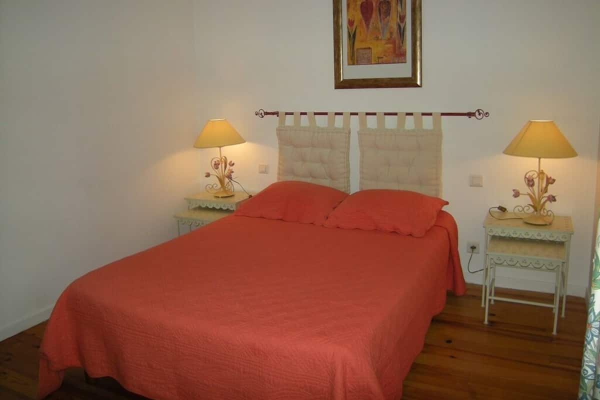 A bedroom with a bed, two bedside tables with lamps, a wall-mounted curtain rod, and a framed picture above the bed.
