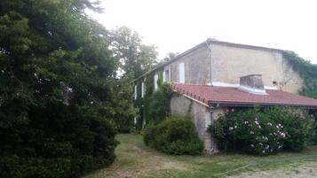A building with a red-tiled roof, surrounded by greenery and a gravel path.