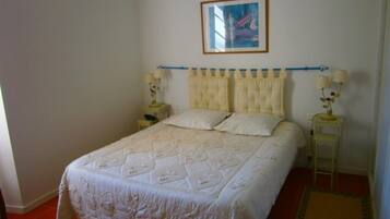 A bedroom with a large bed, two bedside tables, a framed picture on the wall, and a window with curtains.