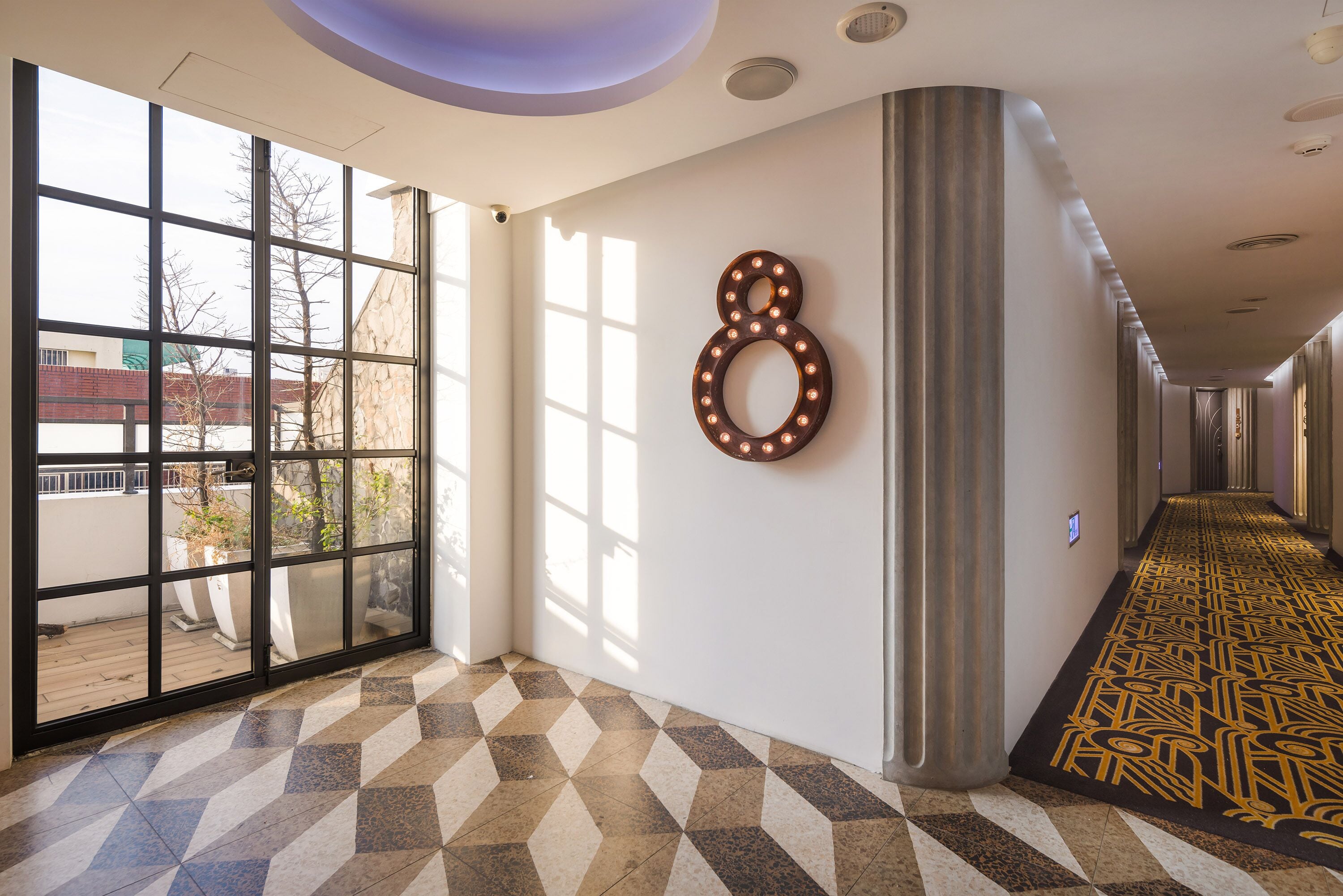 A hotel corridor with patterned flooring, large windows, and a decorative wall number.