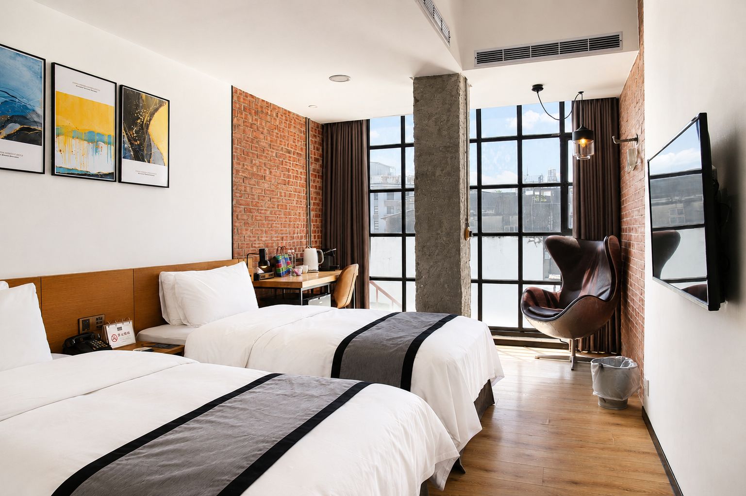 A hotel room with two beds, a desk, a chair, a TV, and large windows with a view.
