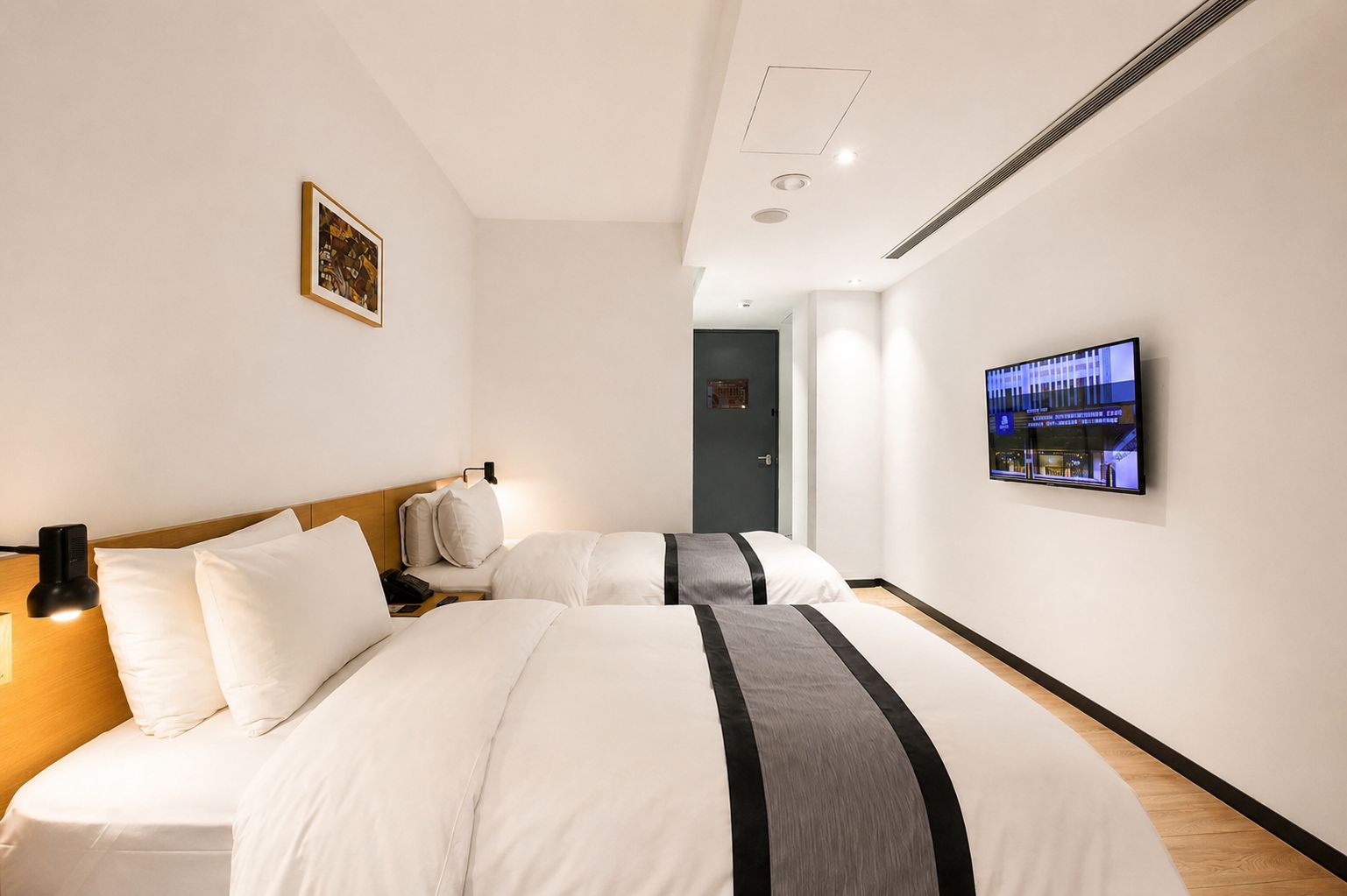 A hotel room with two beds, a flat-screen TV mounted on the wall, and a door leading to another room.