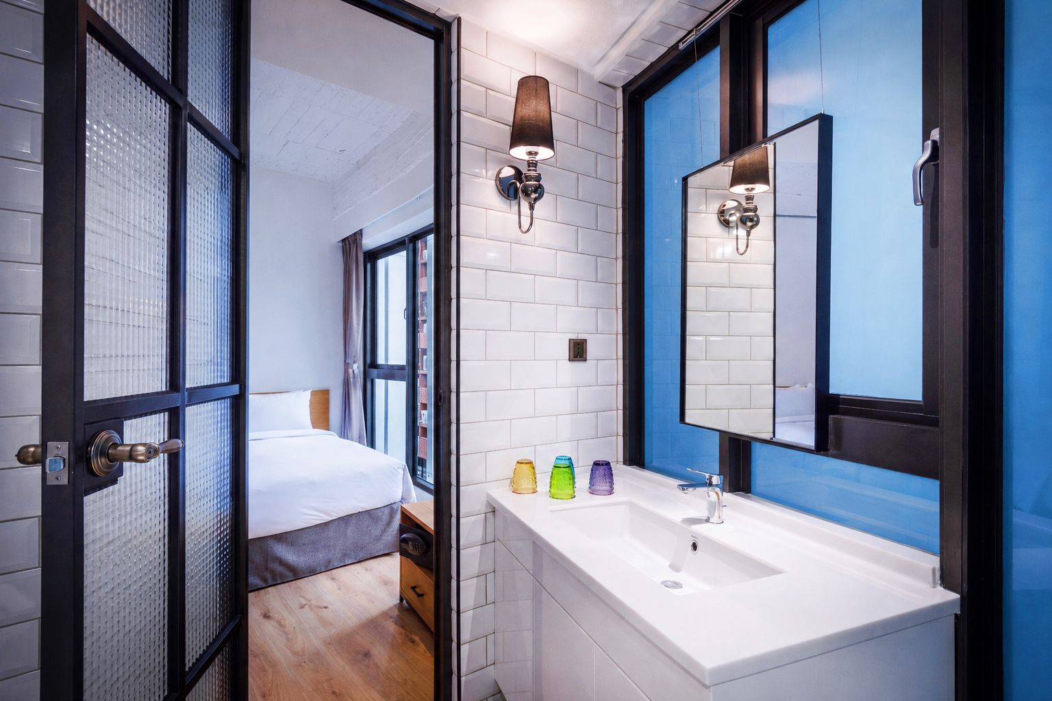 Une salle de bain moderne avec un lavabo blanc, un miroir et une fenêtre dotée de vitres teintées en bleu.