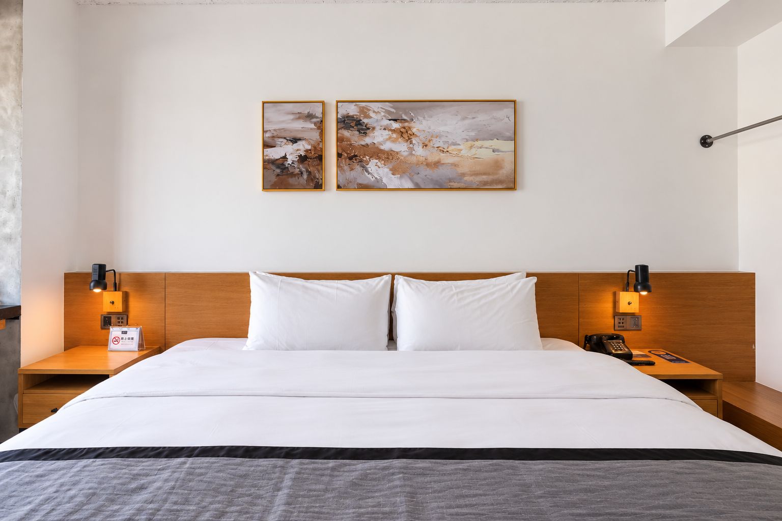 Habitación de hotel con una cama grande, dos mesitas de noche, un cabecero de madera y dos cuadros colgados en la pared.