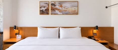 Habitación de hotel con una cama grande, dos mesitas de noche, un cabecero de madera y dos cuadros colgados en la pared.
