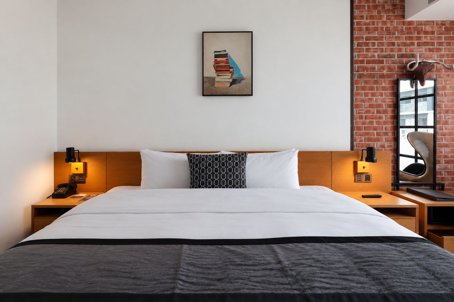 A hotel room with a large bed, two bedside tables, a nightstand, a framed artwork above the bed, a brick wall, and a window.