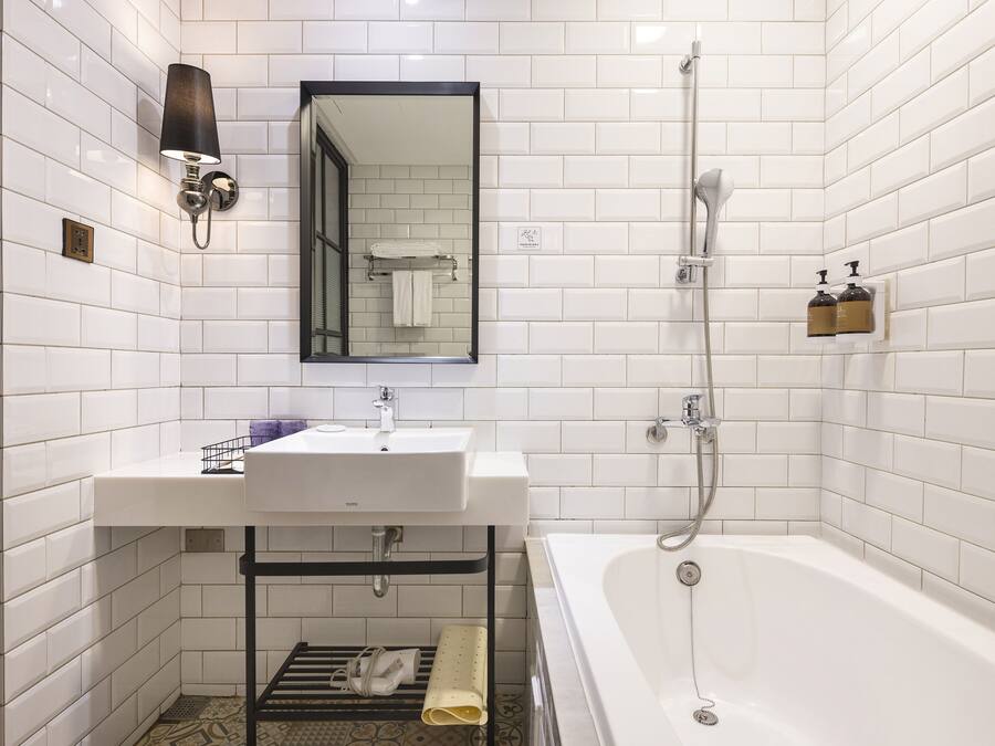 A modern bathroom with white subway tiles, a white sink, a mirror, a shower, and a towel rack.
