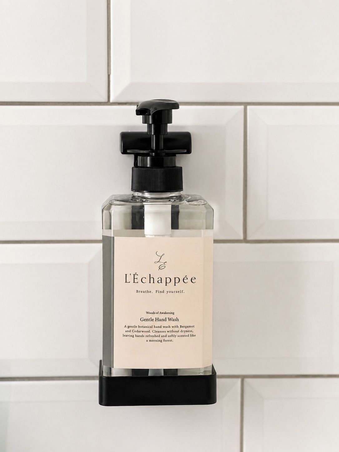 A bottle of L'Echappée Gentle Hand Wash with a black pump dispenser, placed on a white tiled surface.