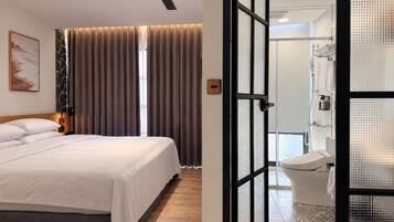 A hotel room with a bed, curtains, a painting, and a bathroom with a toilet and shower.