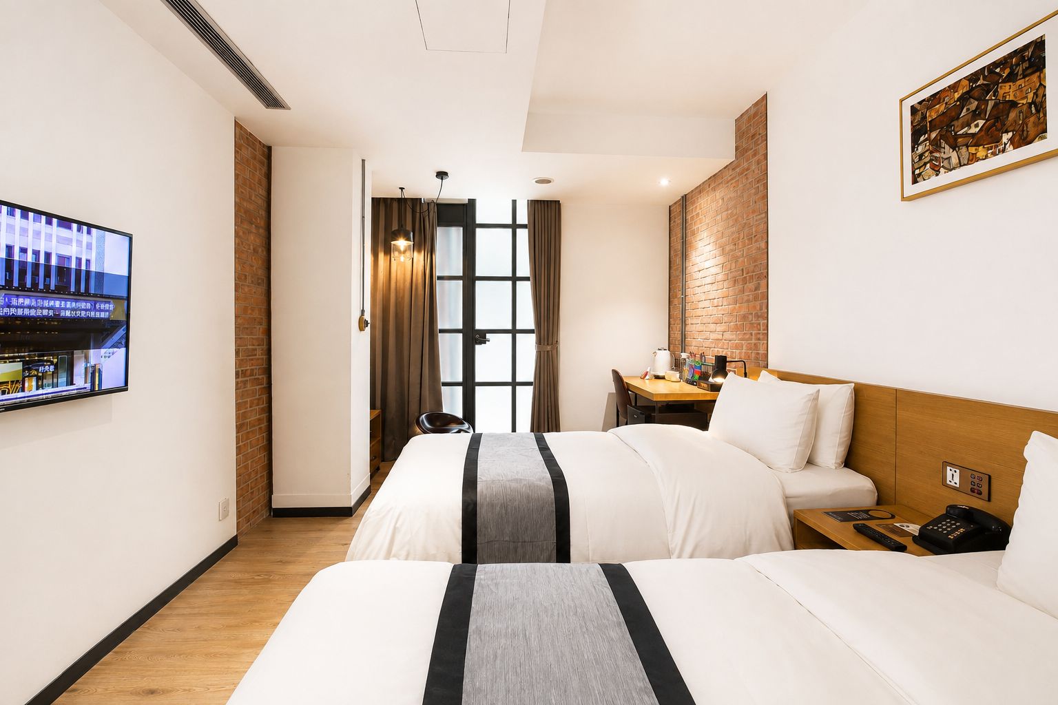 A hotel room with two beds, a desk, a TV, and a brick accent wall.