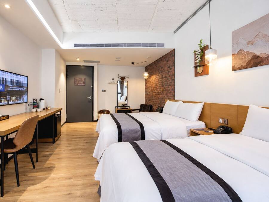 Habitación de hotel con escritorio, dos camas, televisor y una pintura de paisaje de montaña.