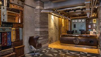 A lobby with vintage suitcases stacked against the wall, a modern reception desk, and a geometric patterned floor.