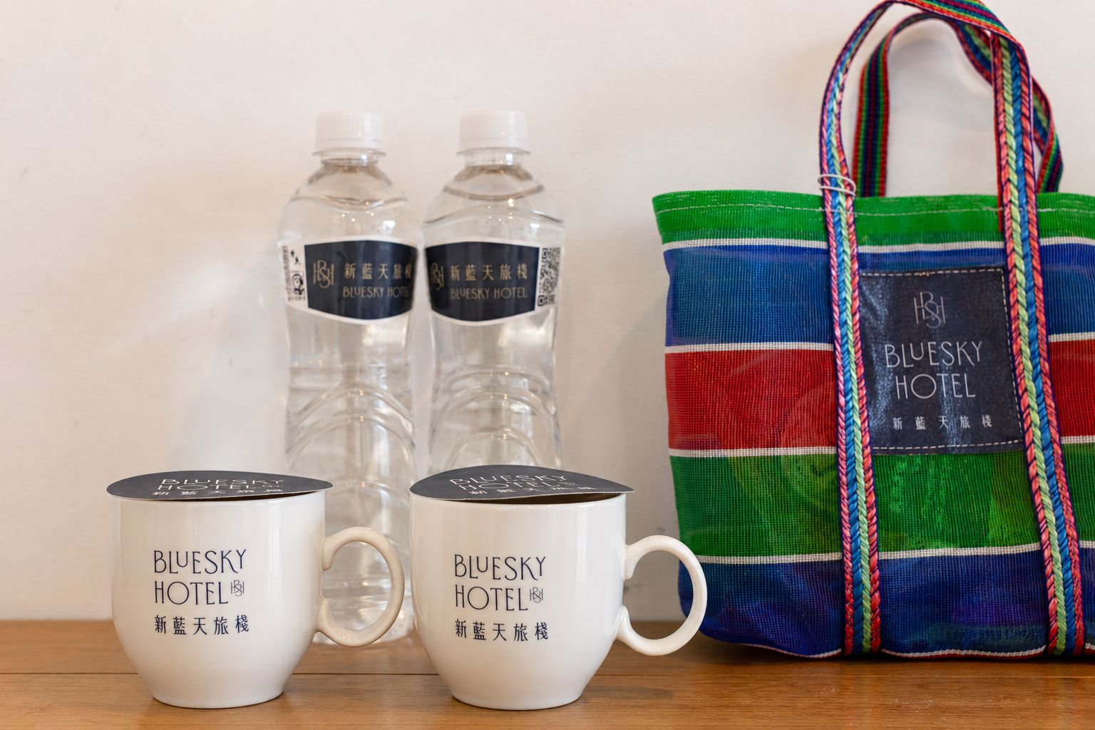 Two white mugs with 'Bluesky Hotel' branding, two clear water bottles, and a colorful striped tote bag with the same branding.