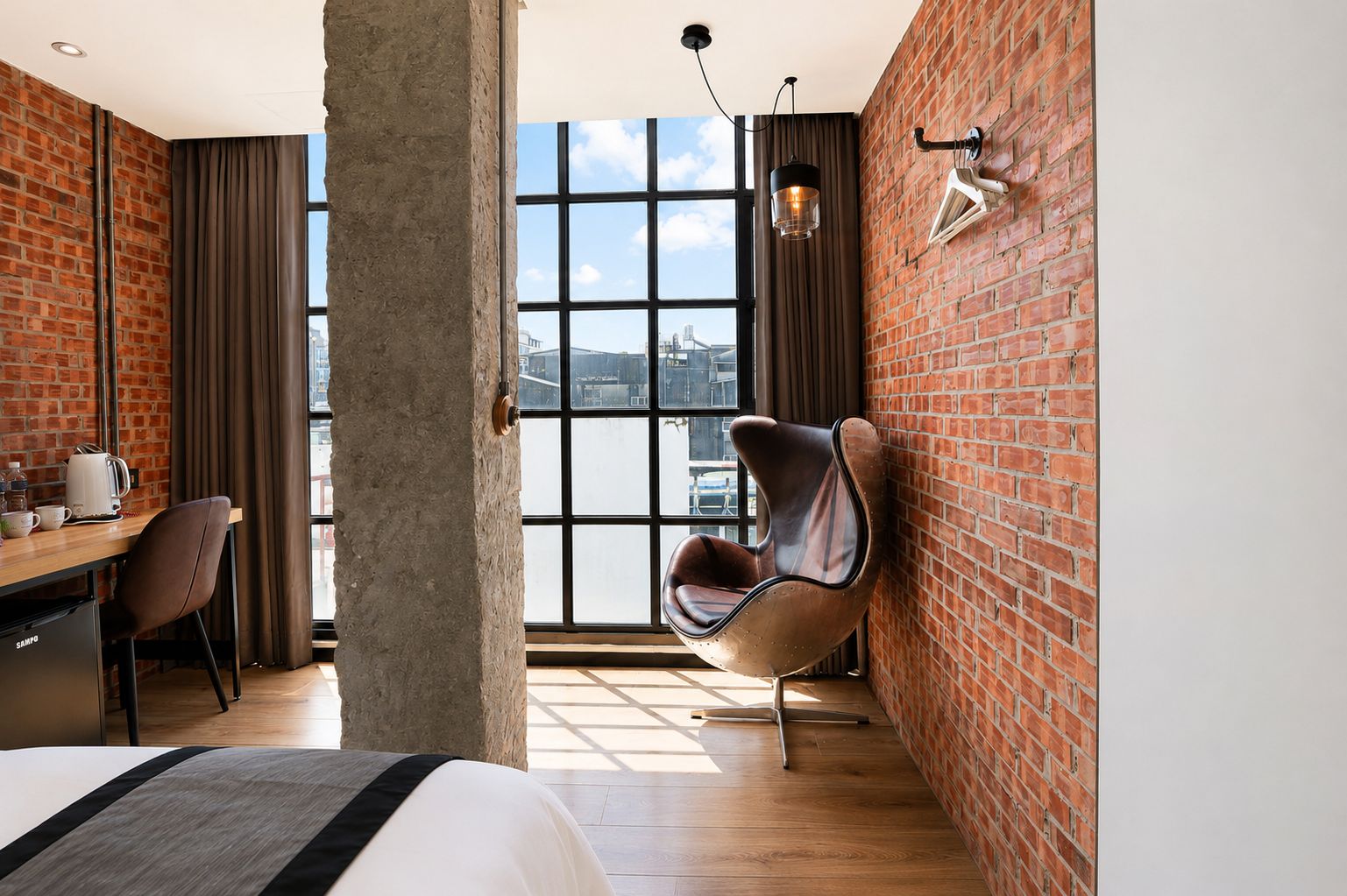 Habitación de hotel con un ventanal grande, una cama, un escritorio con una silla y una original silla curvada.