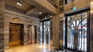 Un interior con tres puertas de ascensor, suelo de mármol y vista de la calle a través de un ventanal.