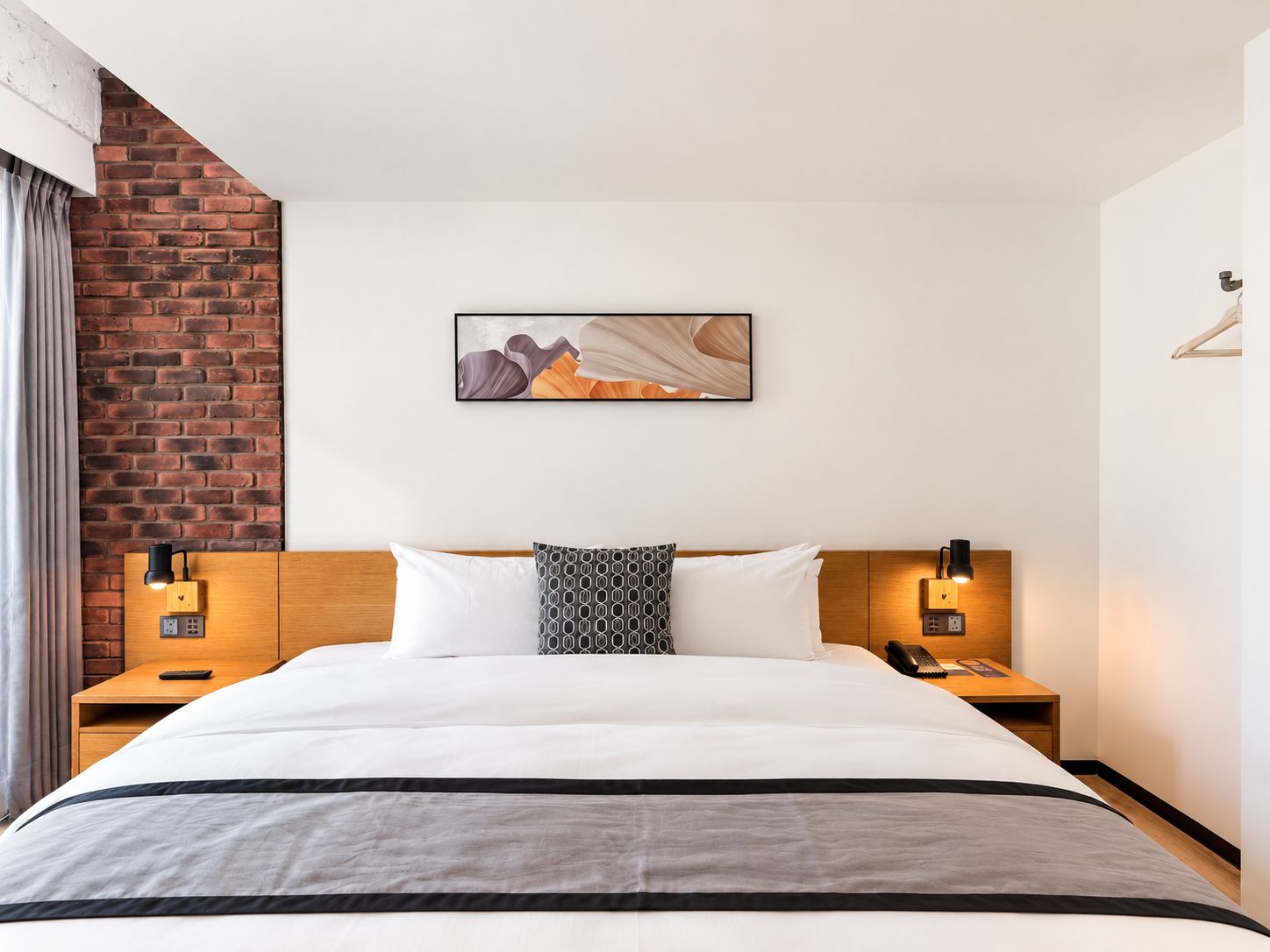 A hotel room with a large bed, a brick accent wall, a painting above the bed, and bedside lamps.