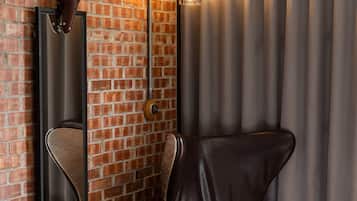 A modern hotel room with a brick wall, a leather chair, a wooden side table, a mirror, and a curtain.