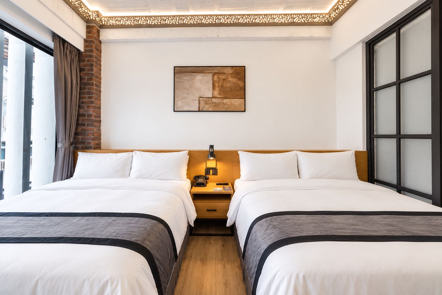 Habitación de hotel con dos camas, una pared de ladrillo decorativa, un cuadro y un ventanal grande.