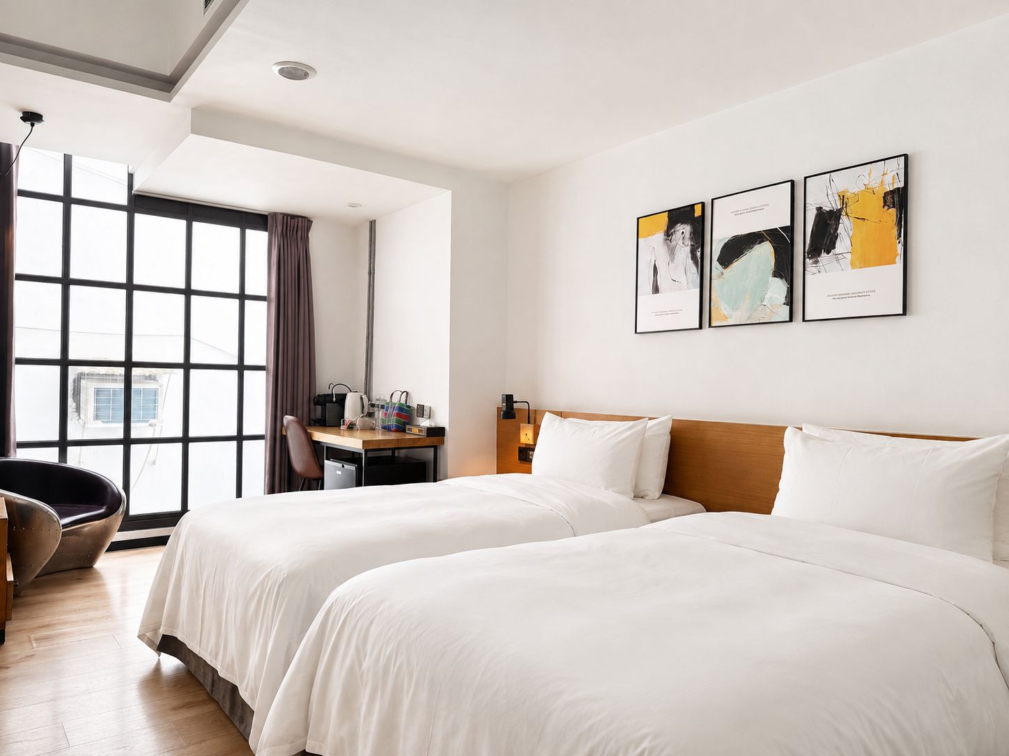A hotel room with two beds, a desk, and a chair. There are three framed pictures on the wall.