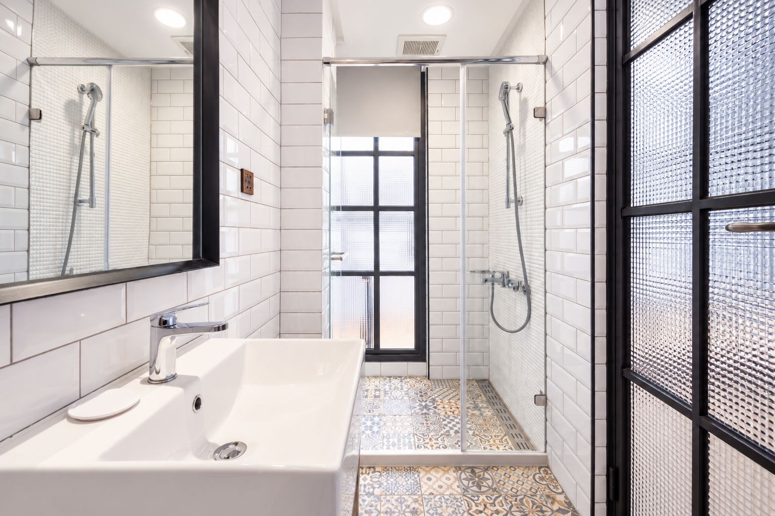 Un baño moderno con un lavamanos blanco, una ducha y un vidrio que da a un balcón.