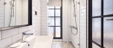 Un baño moderno con un lavamanos blanco, una ducha y un vidrio que da a un balcón.