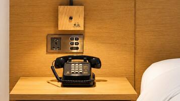 A wooden bedside table with a black telephone, a control panel, and a wall-mounted light fixture.
