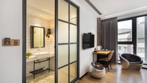 A modern bathroom with a large mirror, sink, and toilet. There is a TV mounted on the wall and a dining area with a table and chairs. - BlueSky Hotel (Taichung)