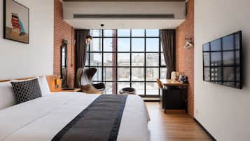A hotel room with a large bed, a desk, a chair, a TV, and a window with a city view.