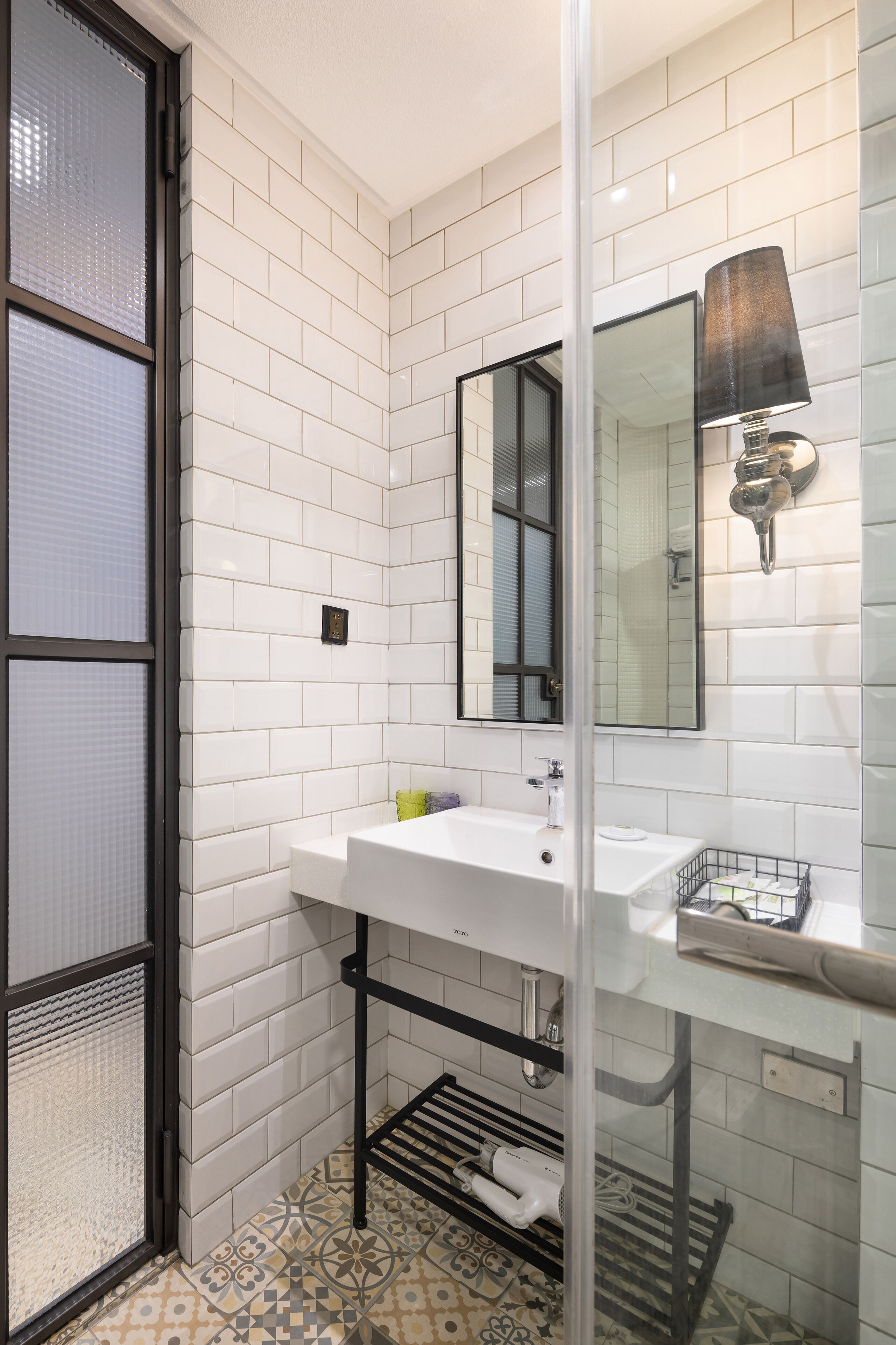 Une salle de bain moderne avec des carreaux de céramique blancs rectangulaires, un lavabo blanc, un miroir et un porte-serviettes noir.