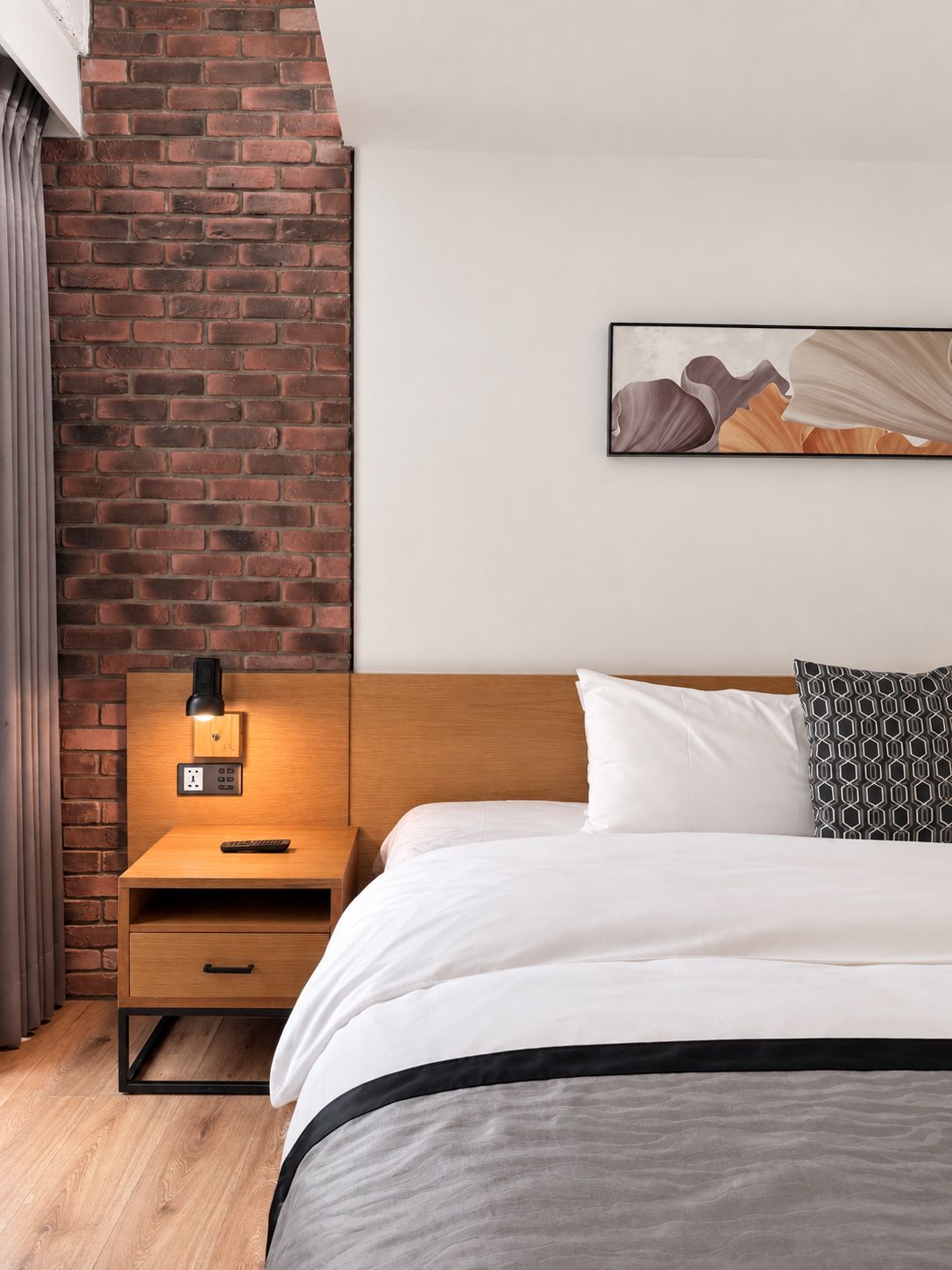 Ein Hotelzimmer mit Backsteinwand, einem Bett mit weißer Bettwäsche, einem Nachttisch mit Lampe und einem Gemälde an der Wand.