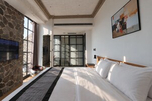 A hotel room with a large bed, a stone wall, a television, and a sliding glass door leading to a balcony.