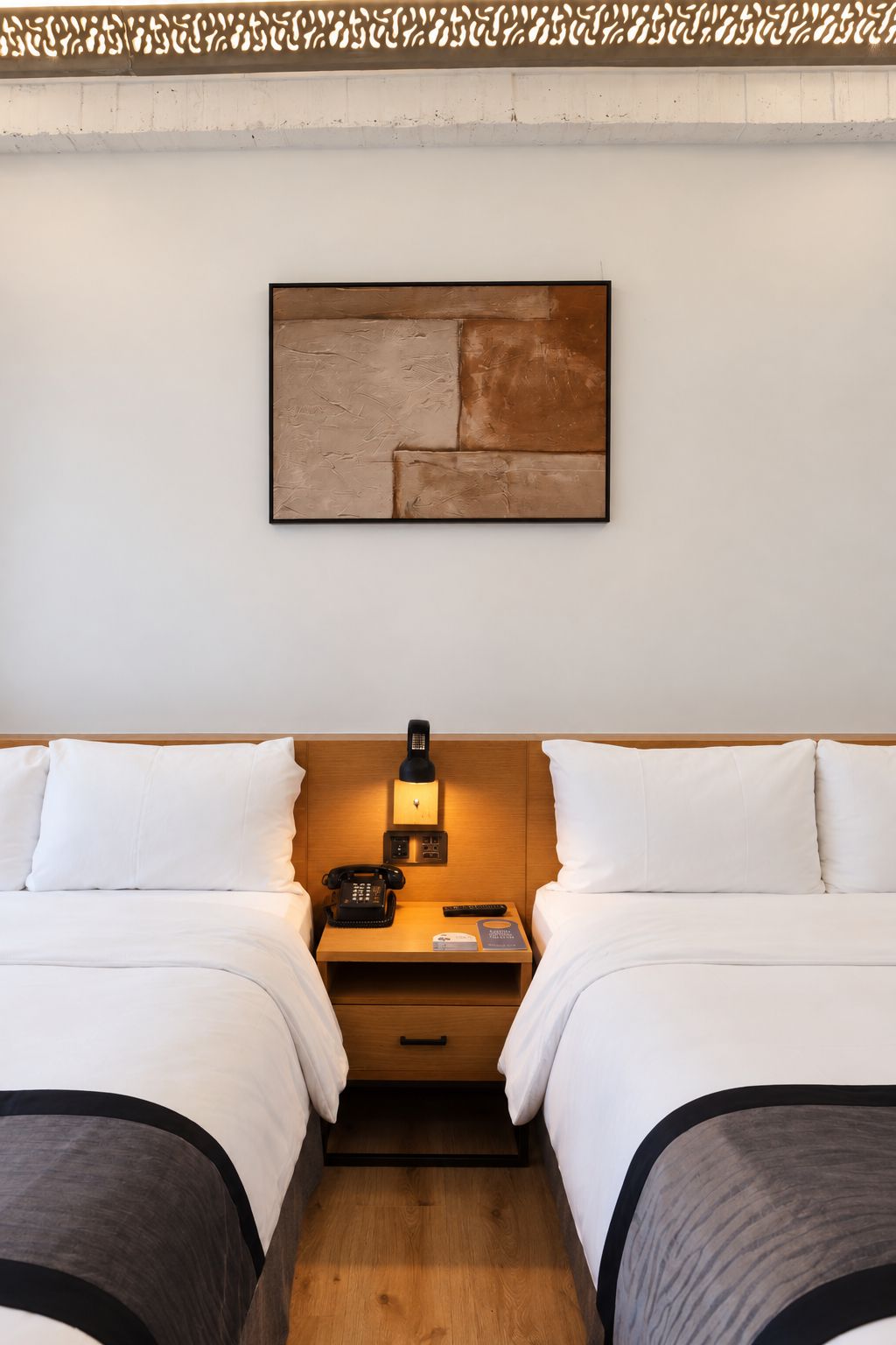 Ein Hotelzimmer mit zwei Betten, einem Nachttisch mit Lampe, einem Telefon und einem kleinen Tisch mit Fernbedienung.