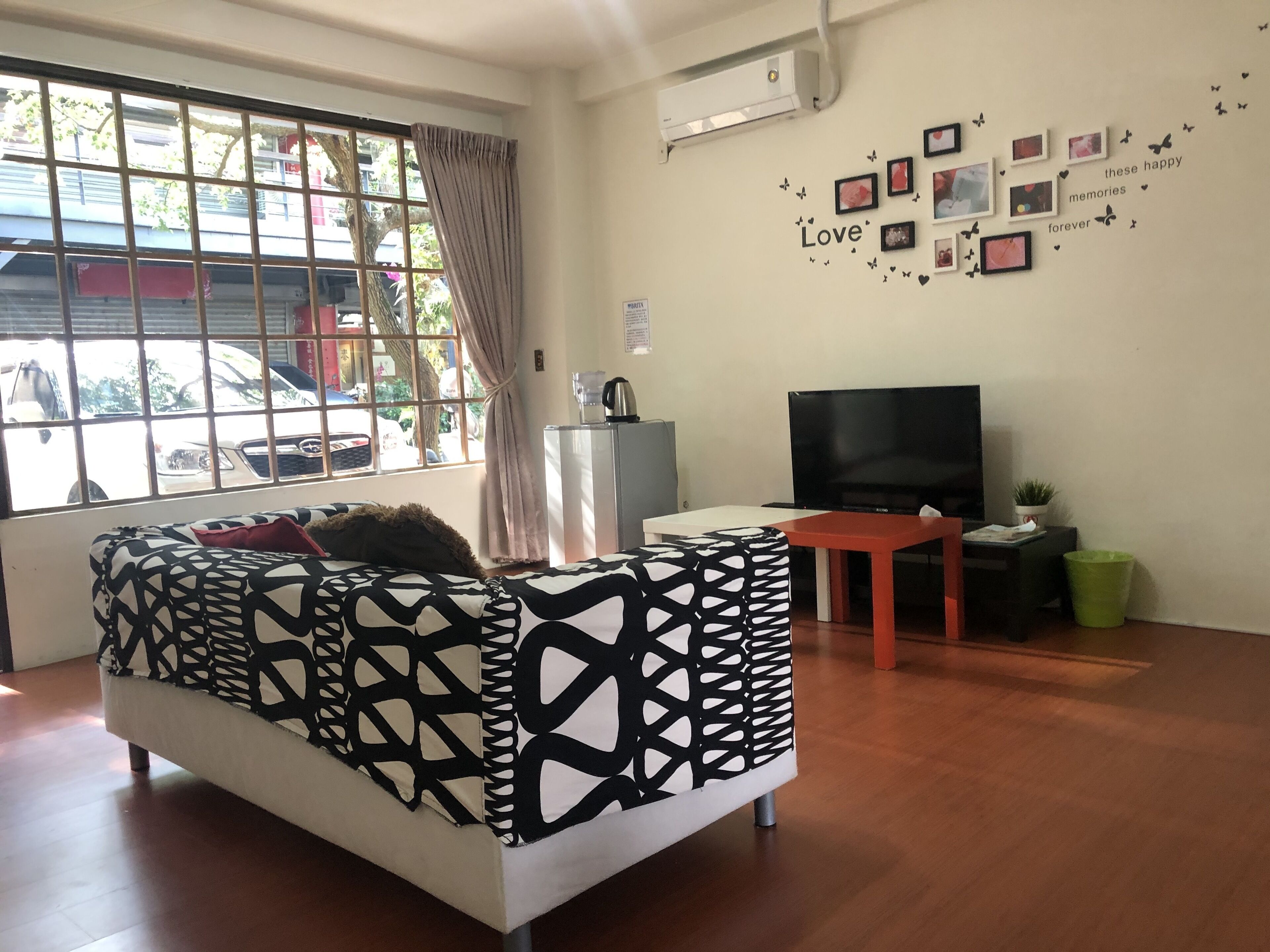 A modern living room with a patterned sofa, a flat-screen TV, and a window with a view of parked cars.